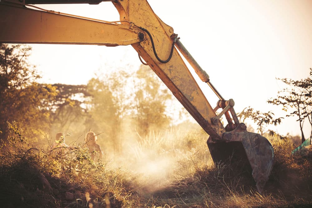 Excavator working at a construction site with sunlight and dust in the background.